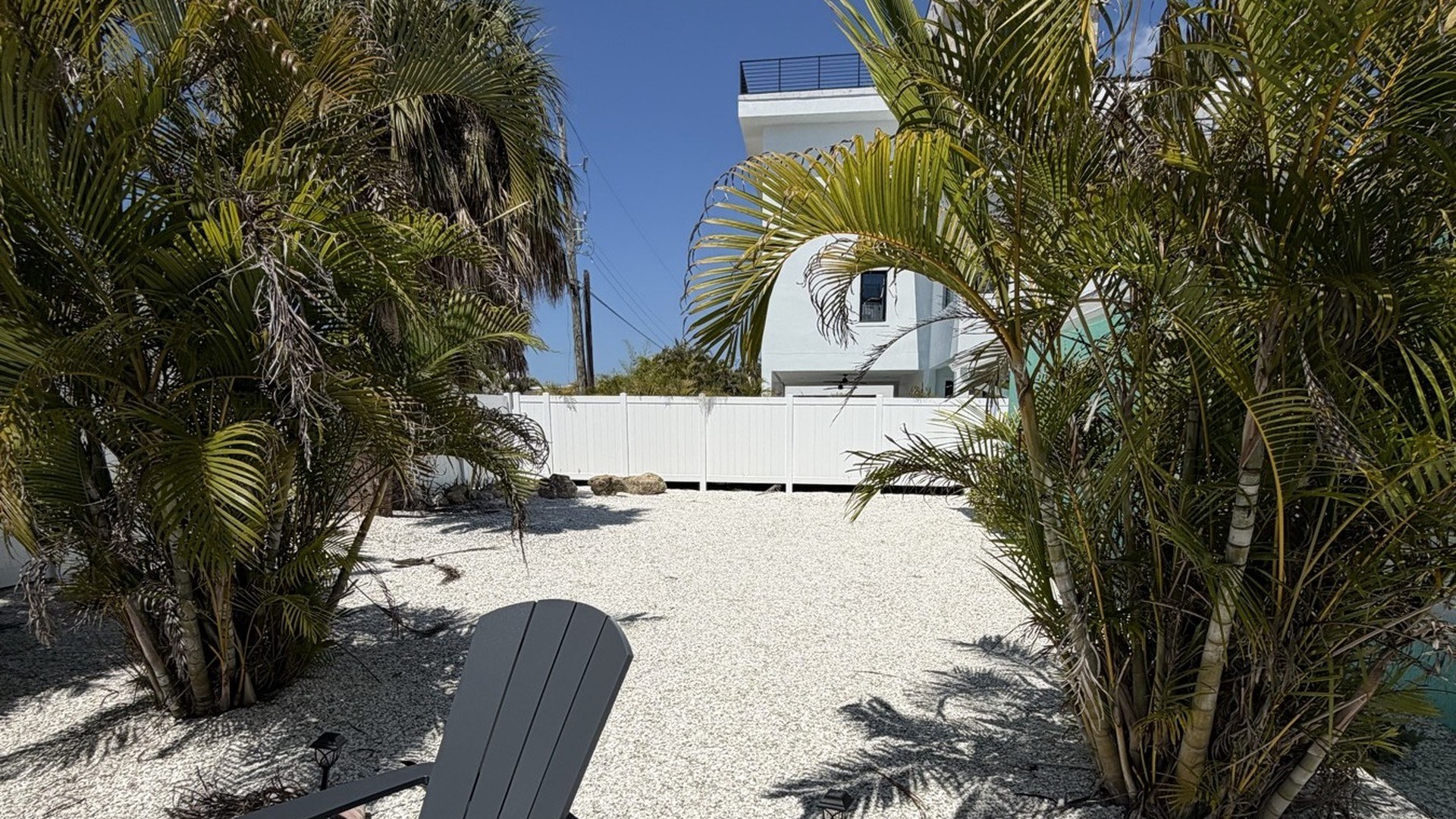 White Adirondack chairs and palms beside the turquoise cottage