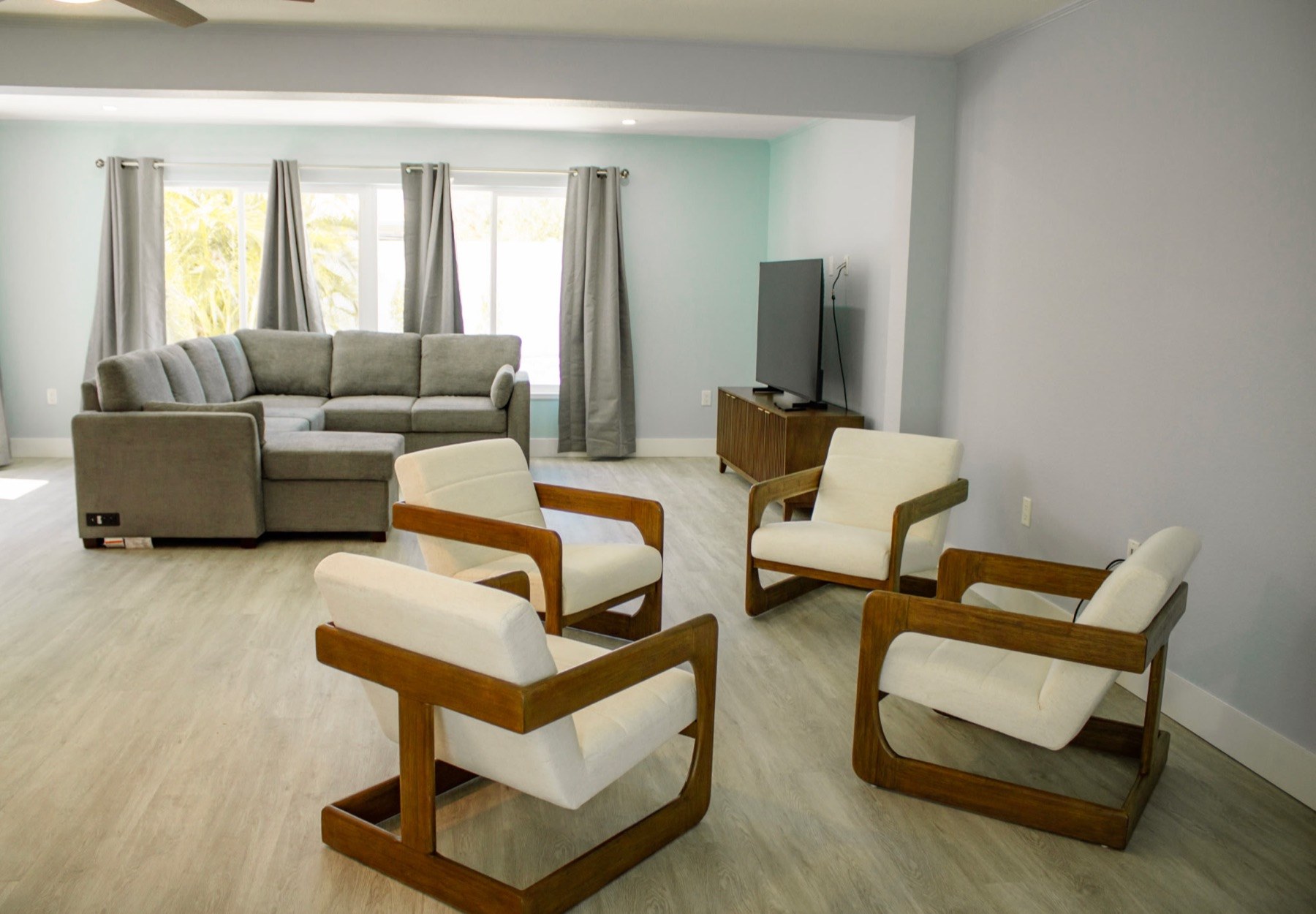 Open living room with gray sofa, cream chairs, and light wood floors